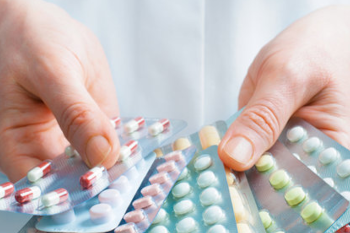 A pair of hands holding a range of pills in blister packes.